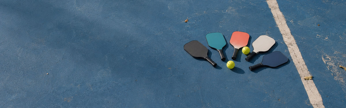 Pickleball paddles in assorted colors fanned out on an outdoor court