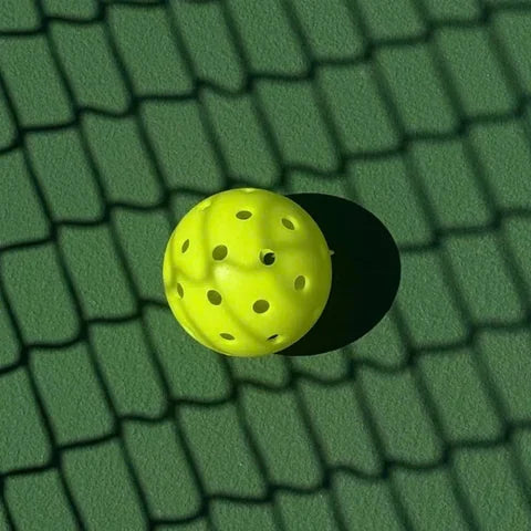 Yellow pickleball resting in the net shadow on a green court
