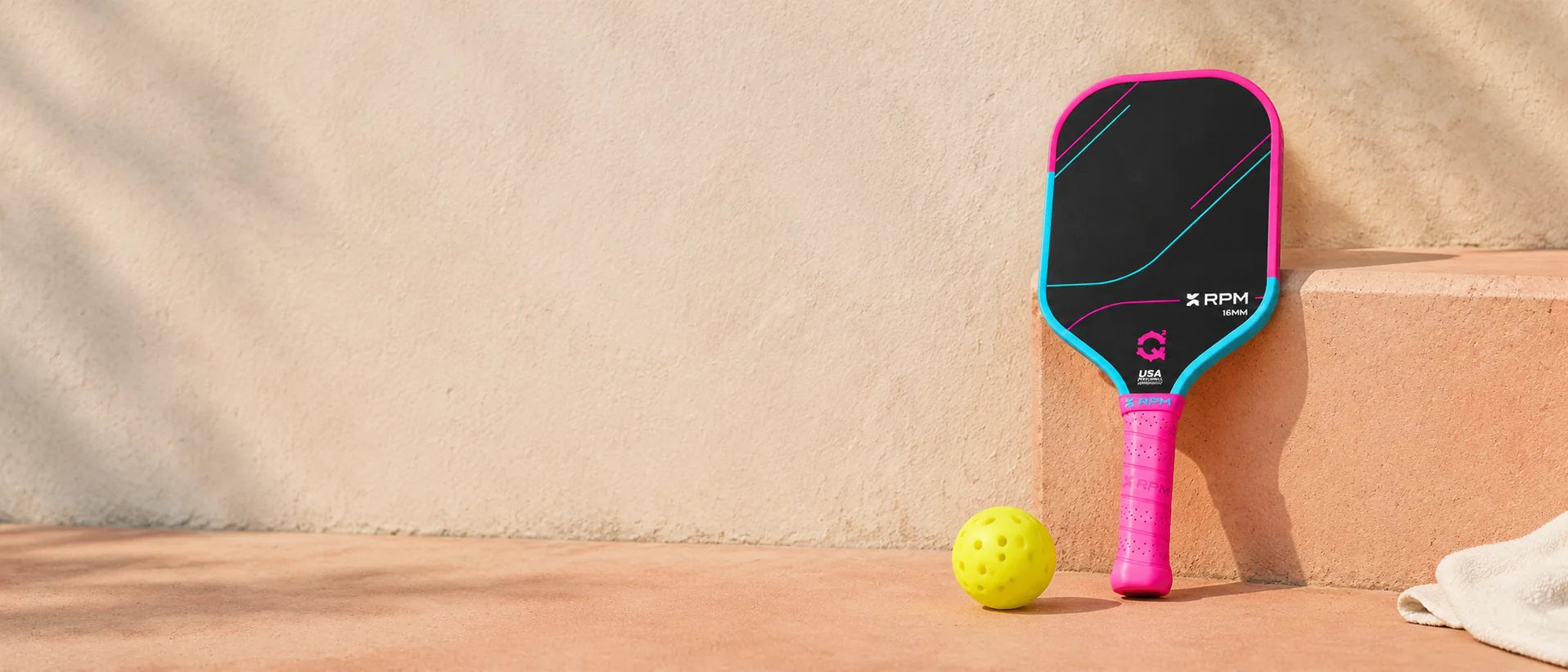 RPM Q2 Cotton Candy paddle and a court ball on a warm peach court step