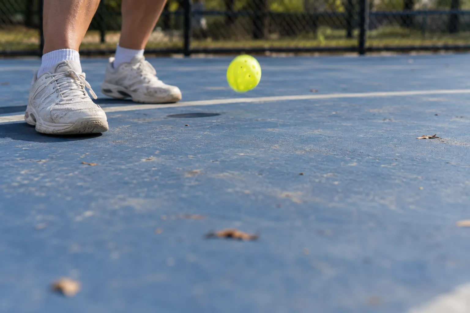 Court shoes at the baseline as a pickleball bounces