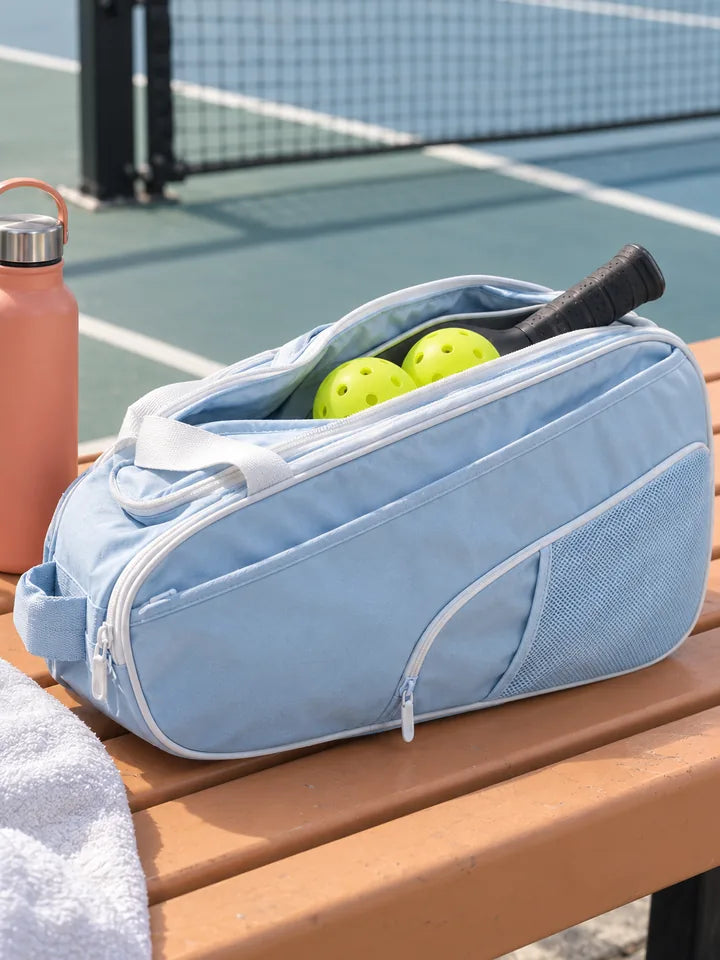Light blue pickleball bag packed with a paddle and balls on a courtside bench
