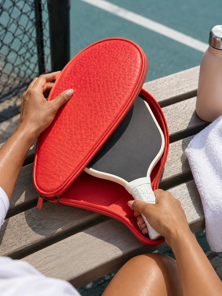Hands sliding a paddle into a coral red paddle case